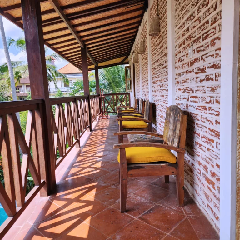 Rustic balcony with wooden furniture overlooking lush tropical greenery.