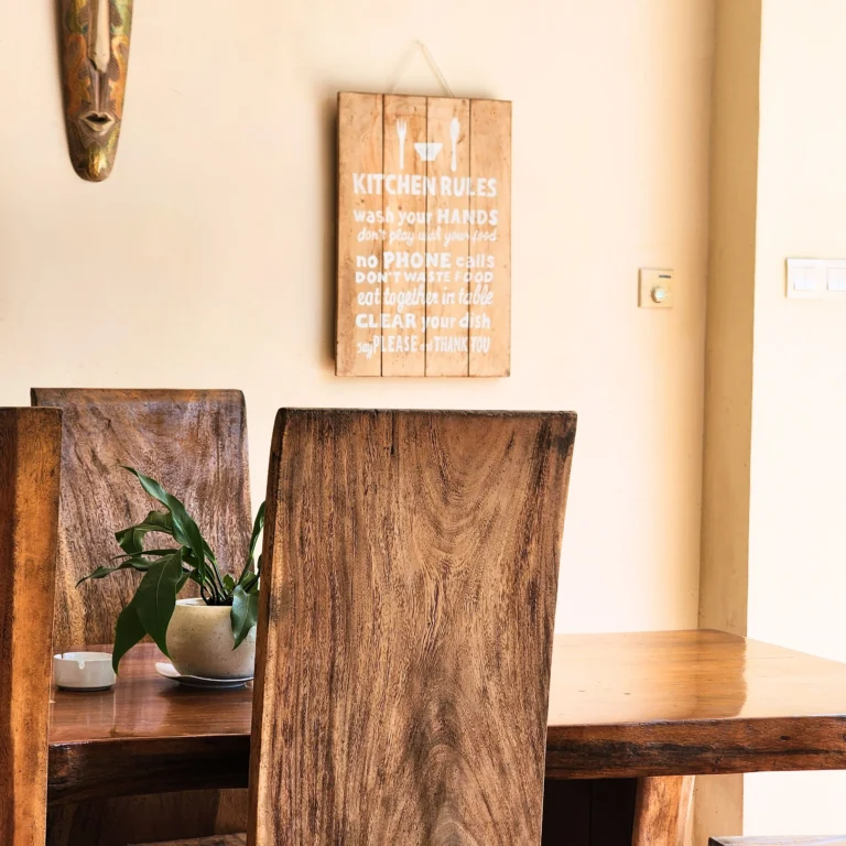 Rustic dining corner with wooden table, potted plant, kitchen rules sign, and tribal wall decor.